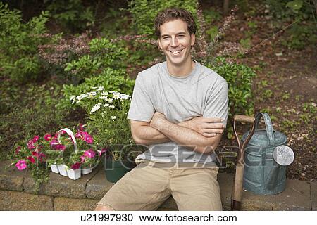 Gardener sitting by flowers and watering can (portrait) View Large Photo Image Stock Image - Gardener sitting by flowers and watering can (portrait). Fotosearch
