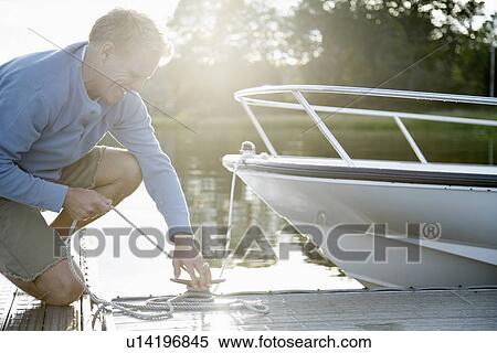 Man tying motorboat to dock View Large Photo Image Stock Photography - Man tying motorboat to dock. Fotosearch