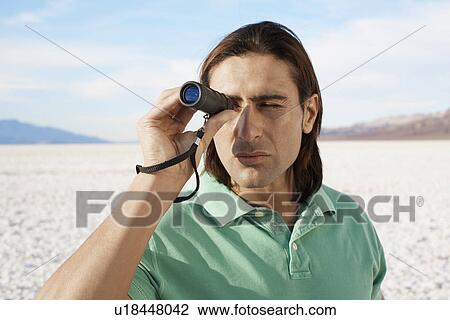 Stock Image - Man using monocular in desert. Fotosearch