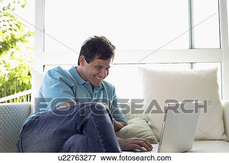 Stock Photo - Mature man using laptop on sofa. Fotosearch