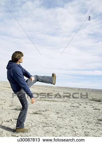 Stock Image - Mid adult man kicking beer can in desert. Fotosearch