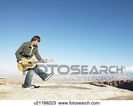 Mid adult man playing acoustic guitar, rock strata in background View Large Photo Image Stock Image - Mid adult man playing acoustic guitar, rock strata in background. Fotosearch