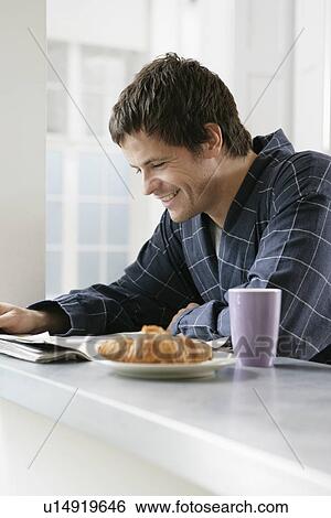 Mid adult man reading newspaper at kitchen counter View Large Photo Image Stock Photograph - Mid adult man reading newspaper at kitchen counter. Fotosearch