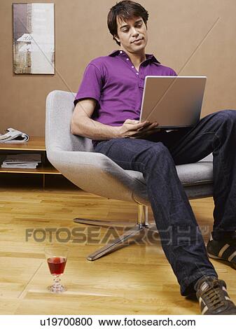 Mid adult man using laptop on armchair View Large Photo Image Stock Image - Mid adult man using laptop on armchair. Fotosearch