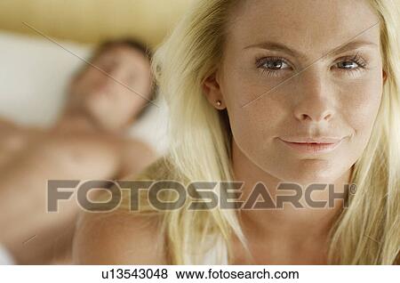 Blond young woman with man lying on bed in background View Large Photo Image Stock Photo - Blond young woman with man lying on bed in background. Fotosearch
