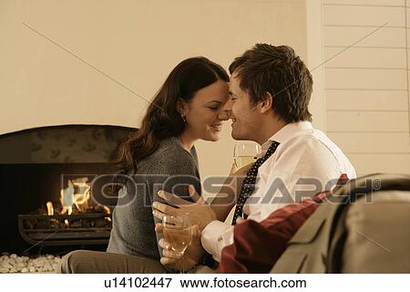 Stock Photo - Mid adult couple drinking wine by fireplace. Fotosearch