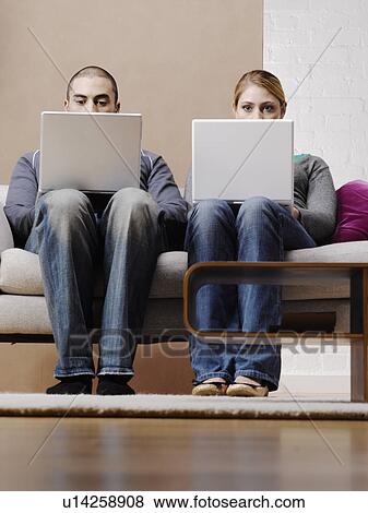 Young couple using laptops on sofa, low angle view View Large Photo Image Stock Photo - Young couple using laptops on sofa, low angle view. Fotosearch