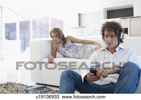 Young man listening to MP3 player, woman reading magazine on sofa View Large Photo Image Stock Image - Young man listening to MP3 player, woman reading magazine on sofa. Fotosearch