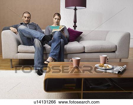 Young woman reading book and young man listening to MP3 player on sofa View Large Photo Image Stock Photograph - Young woman reading book and young man listening to MP3 player on sofa. Fotosearch