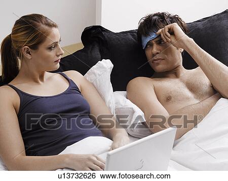 Young woman using laptop in bed, frustrated boyfriend lying next to her View Large Photo Image Stock Photograph - Young woman using laptop in bed, frustrated boyfriend lying next to her. Fotosearch