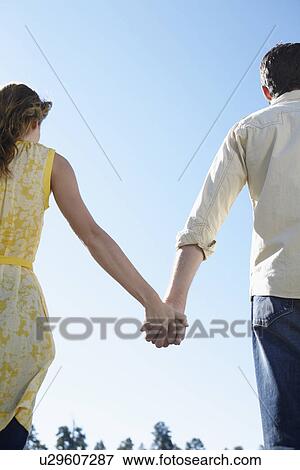 Stock Photo - Young couple holding hands (rear view, low angle view). Fotosearch