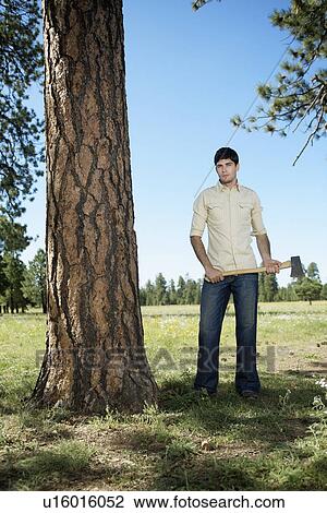 Young man with axe standing by tree View Large Photo Image Stock Image - Young man with axe standing by tree. Fotosearch