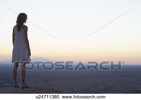 Stock Image - Young woman looking at view at sunset. Fotosearch