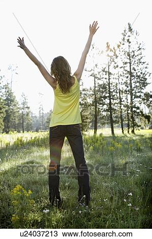 Stock Image - Young woman raising arms in a field of wildflowers. Fotosearch