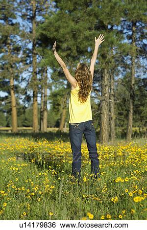Stock Photograph - Young woman raising hands in a field of wildflowers. Fotosearch
