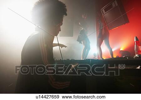 Stock Photo - DJ playing records, dancers in background. Fotosearch