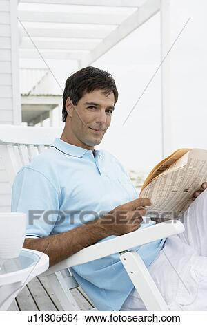 Picture - Mid adult man reading newspaper on lounge chair. Fotosearch