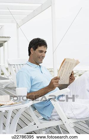 Mid adult man reading newspaper on lounge chair View Large Photo Image Stock Photography - Mid adult man reading newspaper on lounge chair. Fotosearch