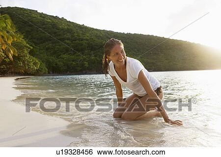 Stock Photograph - Mid adult woman kneeling on sandy beach, St. John, US Virgin Islands, USA. Fotosearch
