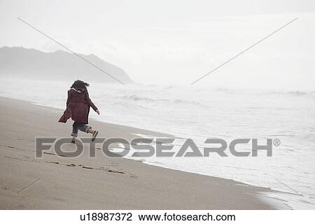 Stock Image - Woman running on sandy beach (rear view). Fotosearch