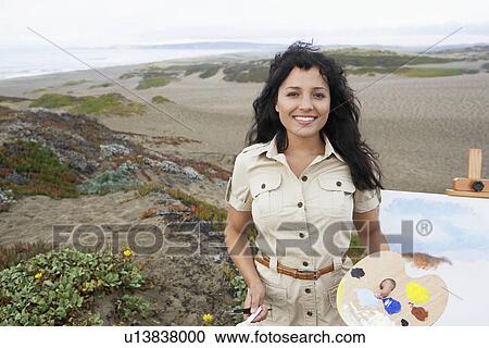 Stock Image - Young woman painting on beach (portrait). Fotosearch