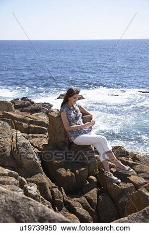 Young woman using mobile phone at rocky beach View Large Photo Image Stock Image - Young woman using mobile phone at rocky beach. Fotosearch