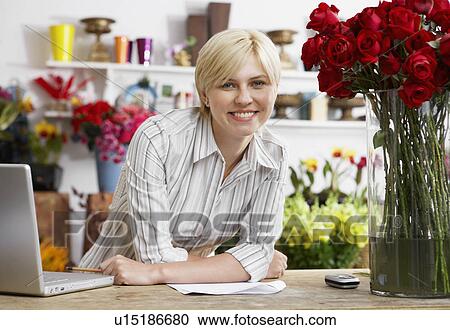 Stock Image - Female florist with laptop leaning on table (portrait). Fotosearch