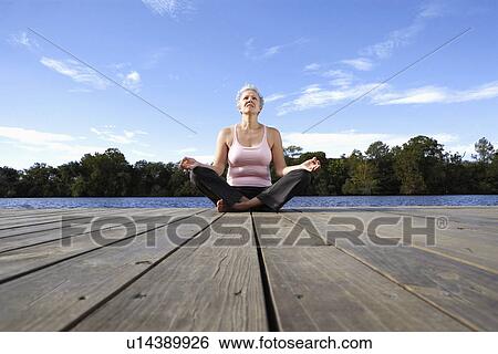 Mature woman meditating in lotus position (low angle view) View Large Photo Image Stock Photograph - Mature woman meditating in lotus position (low angle view). Fotosearch