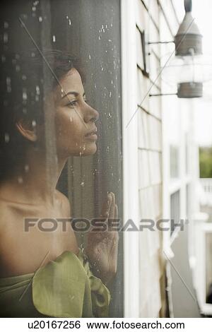 Mid adult woman looking through window with rain running down View Large Photo Image Stock Photograph - Mid adult woman looking through window with rain running down. Fotosearch