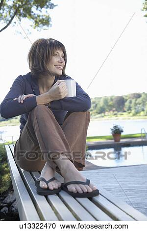 Stock Image - Woman drinking coffee on bench (low angle view). Fotosearch