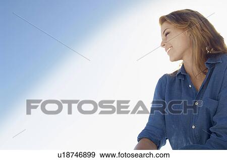 Stock Photo - Young woman against clear sky (portrait, low angle view). Fotosearch