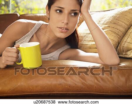 Young woman holding mug and lying on sofa View Large Photo Image Stock Photo - Young woman holding mug and lying on sofa. Fotosearch