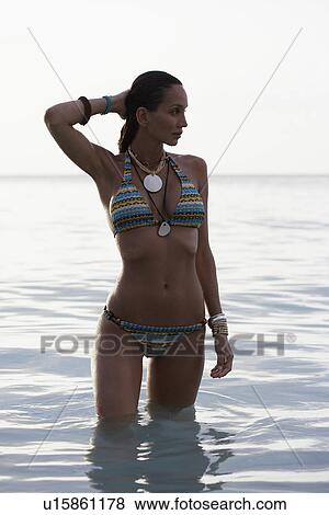 Stock Photo - Young woman in bikini standing in ocean. Fotosearch