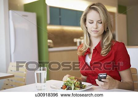 Young woman using cell phone while having lunch View Large Photo Image Stock Photograph - Young woman using cell phone while having lunch. Fotosearch