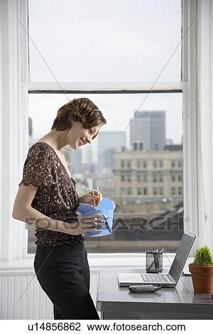 Stock Image - Businesswoman looking at cell phone and eating takeout food. Fotosearch