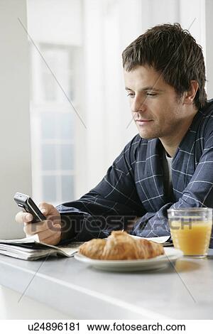 Mid adult man using cell phone at breakfast table View Large Photo Image Stock Image - Mid adult man using cell phone at breakfast table. Fotosearch