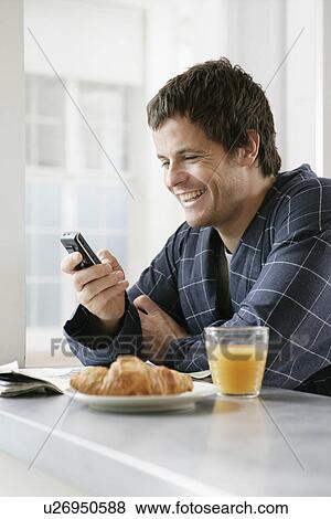 Mid adult man using cell phone at breakfast table View Large Photo Image Stock Photo - Mid adult man using cell phone at breakfast table. Fotosearch
