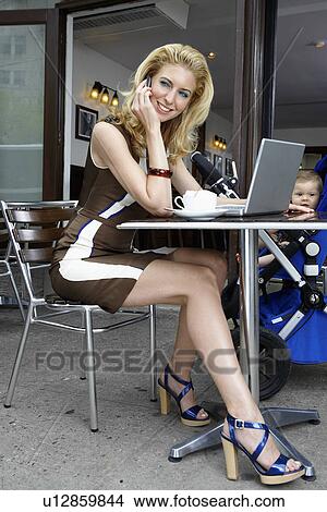 Picture - Mid adult mother with laptop talking on phone. Fotosearch