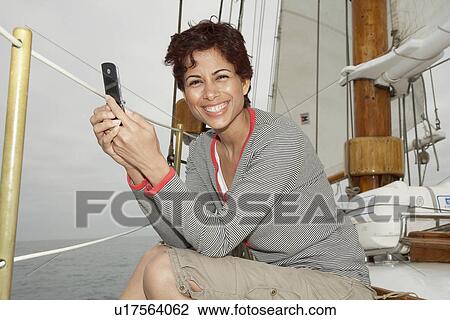 Stock Image - Woman using cell phone in sail boat (portrait). Fotosearch