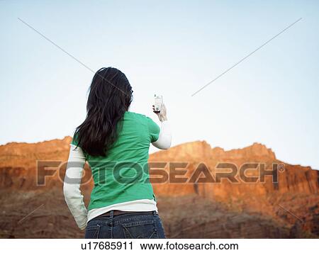 Stock Image - Woman using cell phone near rock strata, rear view. Fotosearch