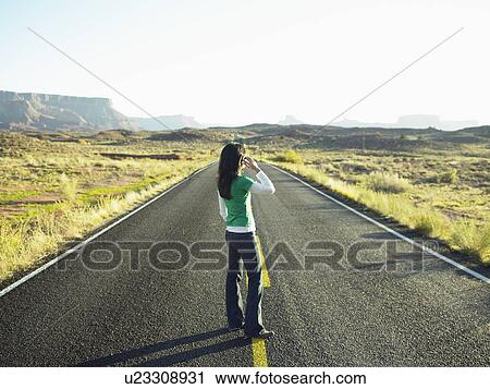 Stock Image - Woman using cell phone on highway, Moab, Utah, USA. Fotosearch