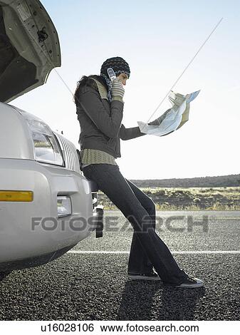 Stock Photograph - Woman with road map talking on cell phone by broken car. Fotosearch