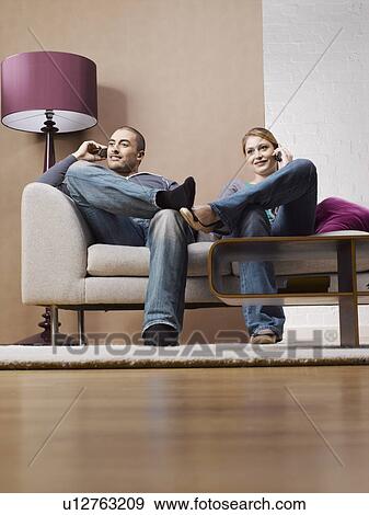 Young couple on cell phones on sofa View Large Photo Image Stock Photo - Young couple on cell phones on sofa. Fotosearch