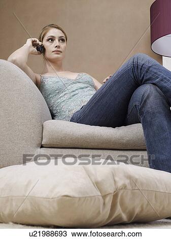 Stock Image - Young woman on cell phone on sofa (low angle view). Fotosearch