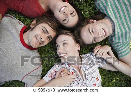 Stock Image - Four friends lying on grass (directly above). Fotosearch