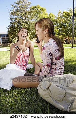 Two young women using cell phones in park View Large Photo Image Picture - Two young women using cell phones in park. Fotosearch