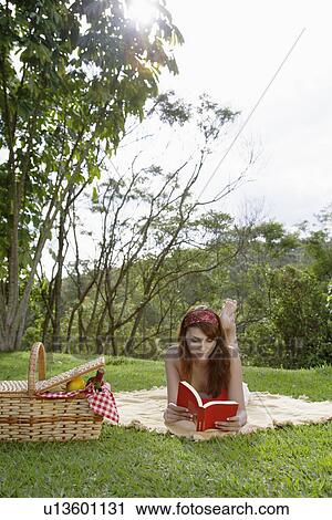 Stock Image - Young woman reading book at picnic. Fotosearch