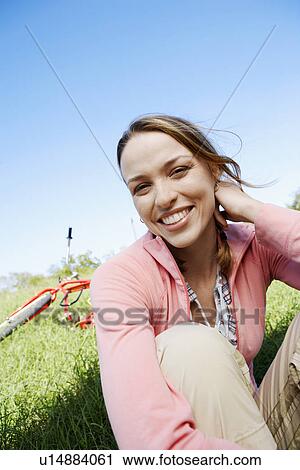 Young woman sitting on lawn, bicycle in background (portrait) View Large Photo Image Stock Image - Young woman sitting on lawn, bicycle in background (portrait). Fotosearch