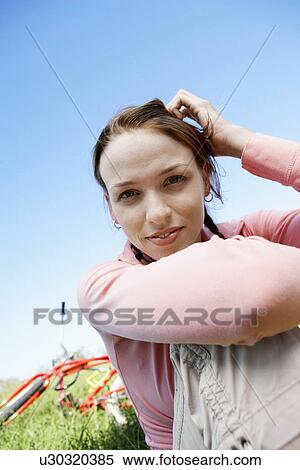 Stock Photography - Young woman sitting on lawn, bicycle in background (portrait, low angle view). Fotosearch