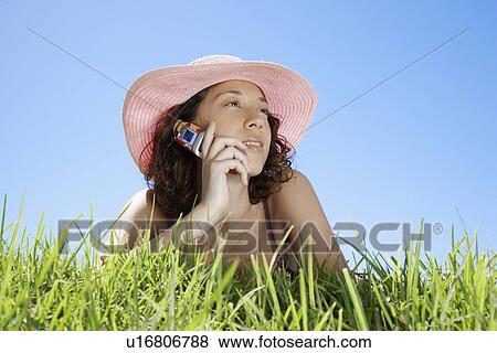 Young woman talking on cell phone and lying on grass (low angle view) View Large Photo Image Stock Photo - Young woman talking on cell phone and lying on grass (low angle view). Fotosearch